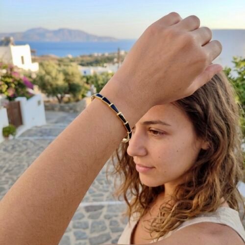 Κομψό χρυσό βραχιόλι χειροπέδα (bangle) με γεωμετρικά διακοσμητικά στοιχεία από μαύρο σμάλτο, φορεμένο σε γυναικείο καρπό.